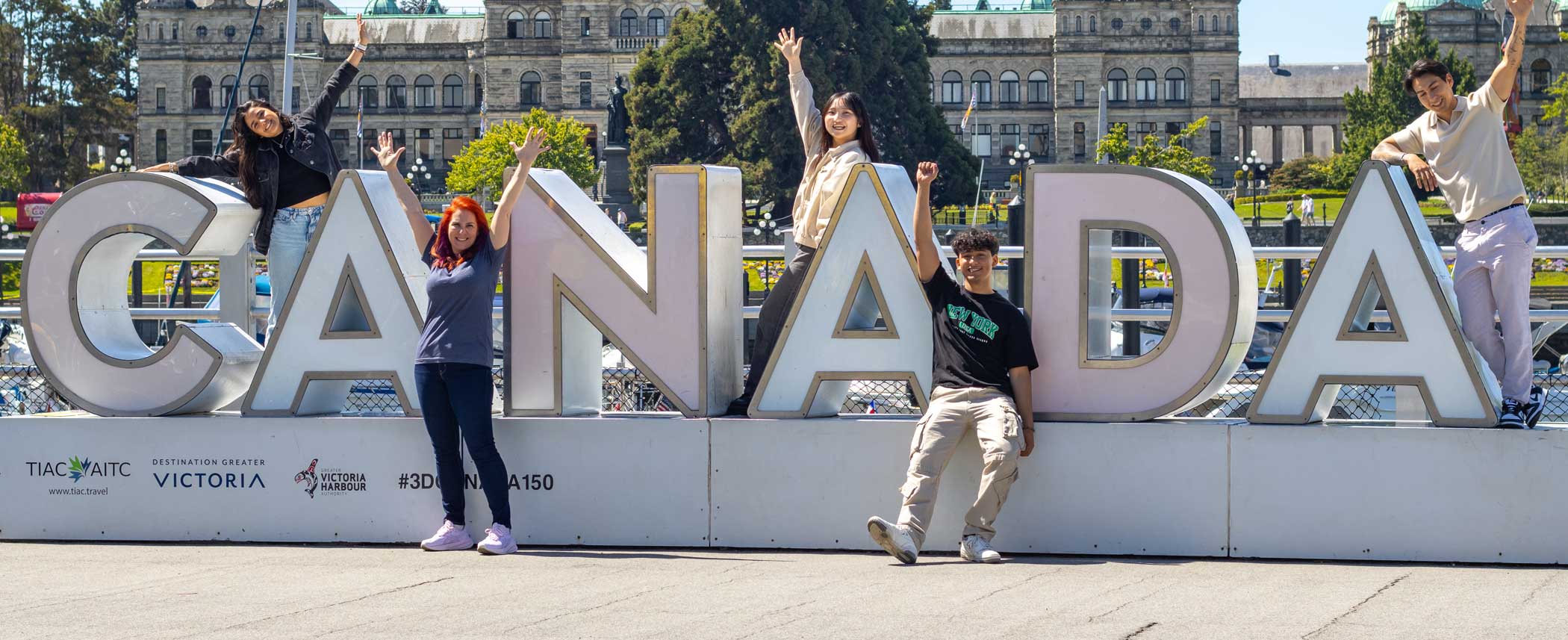 Students who are ready to learn English in Canada standing on large letter sign.
