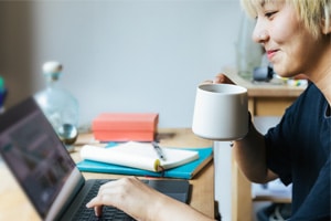 Person drinking coffee and getting ready to learn English Language skills Using a laptop with notepad nearby.